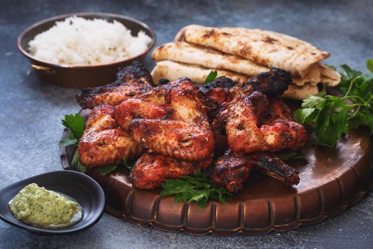 Spicy tandoori chicken wings served with mint chutney dipping sauce, pilau rice and garlic naan, selective focus