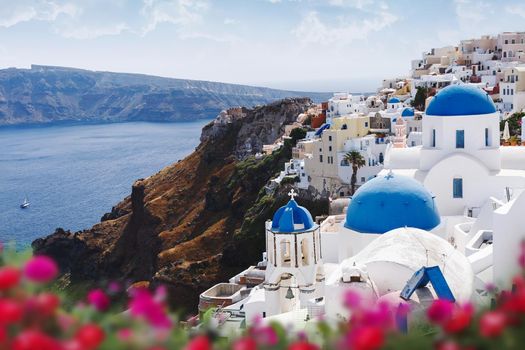 Blue domes, bell tower of churches and flowers in Oia, Santorini, Greece.