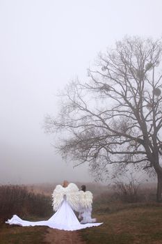 Two girls in angel costumes and white dresses walking in the park. Mother and daughter