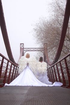 Two girls in angel costumes and white dresses walking in the park. Mother and daughter