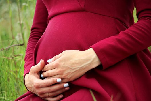 Pregnant woman in red dress holding her belly in the park