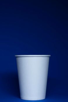 An empty white paper cup on a blue background. vertical photo.