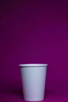 An empty white paper cup on a pink background. vertical photo.