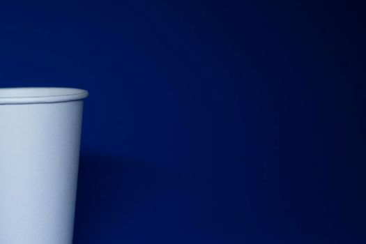 An empty white paper cup on a blue background. horizontal photo.