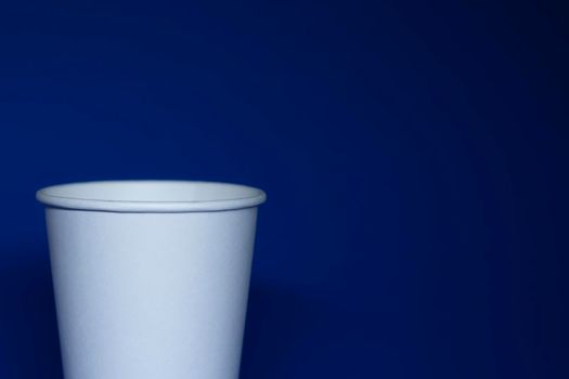 An empty white paper cup on a blue background. horizontal photo.