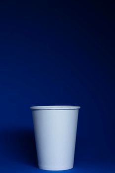 An empty white paper cup on a blue background. vertical photo.