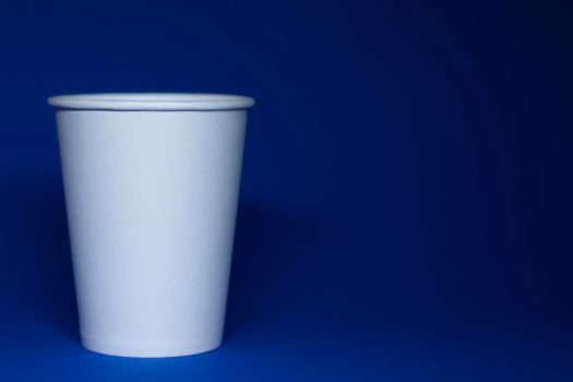 An empty white paper cup on a blue background. horizontal photo.