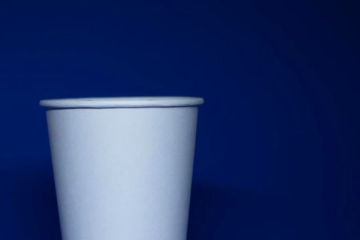 An empty white paper cup on a blue background. horizontal photo.