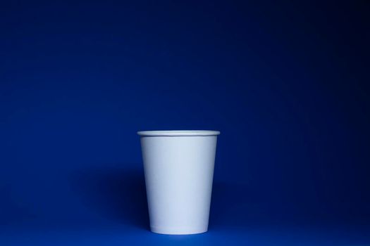 An empty white paper cup on a blue background. horizontal photo.