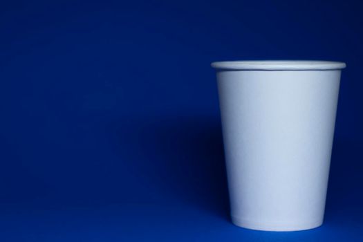 An empty white paper cup on a blue background. horizontal photo.