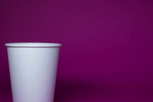 An empty white paper cup on a pink background. horizontal photo.