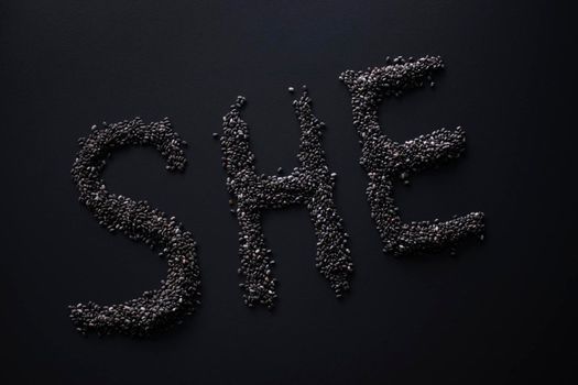 Word 'SHE' written with chia seeds on gray background, top view, copy space.