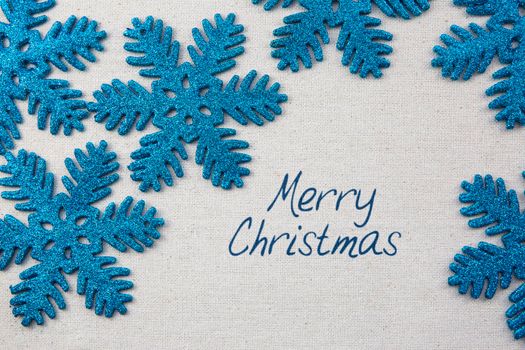 Sparkling blue snowflake ornaments on linen surface with Merry Christmas greeting.