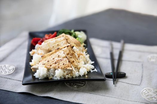Grilled tofu on a bed of rice with veggies and chop sticks.