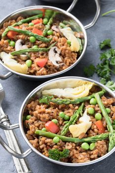 Two bowls of vegan paella with asparagus, mushrooms and artichoke hearts.