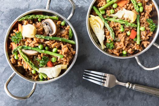 Two bowls of vegan paella with asparagus, mushrooms and artichoke hearts - flat lay.