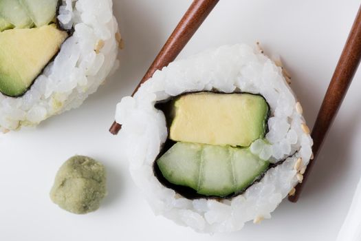 Vegan cucumber and avocado uramaki sushi rolls with wasabi and chop sticks.