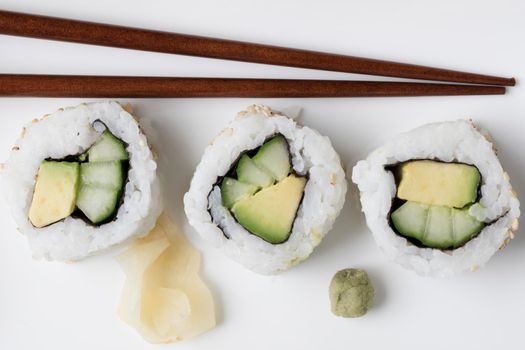 Vegan cucumber and avocado uramaki sushi rolls with wasabi, pickled ginger, and chop sticks.