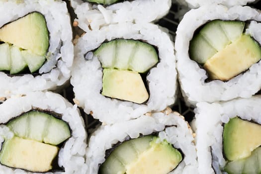 Vegan cucumber and avocado uramaki sushi rolls close up top view.