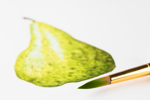 Watercolor brush with green paint in front of painting of a pear.