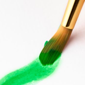 Watercolor paint brush with green paint on paper.