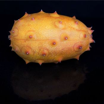 Whole Kiwano fruit on black, with faint reflection