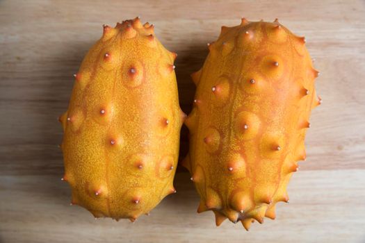 Two whole kiwano fruits on wodden surface from high angle.