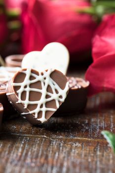 Close up of heart shaped chocolate with red roses in the background.