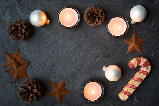 Rustic Christmas decorations and tea lights on dark stone surface with copy space in the center.  Viewed from directly above