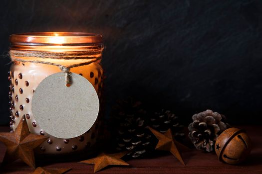 Rustic Christmas scene with jar candle, pine cones, metals stars and round tag with copy space.