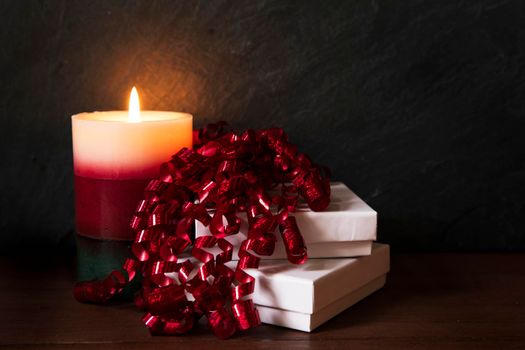 Two gift boxes with curly red ribbon and festive candle.