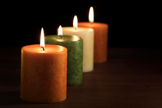 Row of autumn color burning candles angled into black background with copy space.