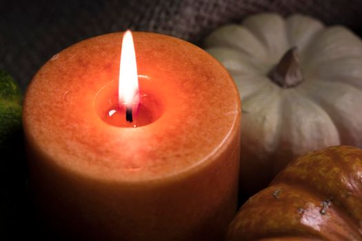 Fall theme close up of orange candle burning with gourds