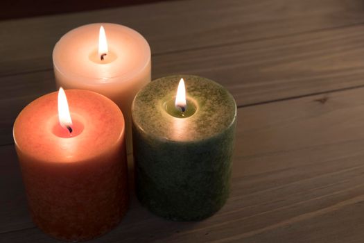 Orange, green and white candles burning on wooden table