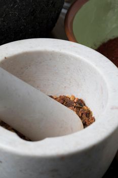 Vertical orientation close up of porcelain mortar and pestle with crushed dried chili pepper.