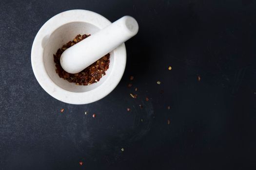 Small porcelain mortar and pestle with dried chili pepper on dark surface with copy space.