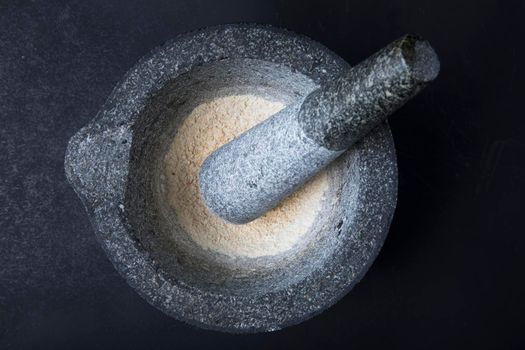 Stone mortar and pestle with dried onion on dark surface.
