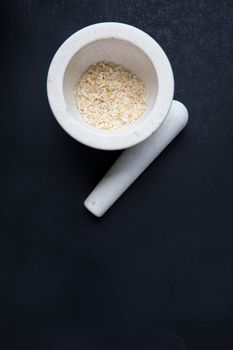 Small porcelain mortar and pestle with dried onion on dark surface and copy space.