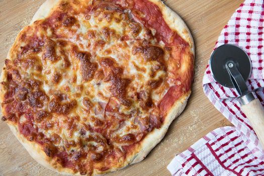 Whole homemade cheese and ham pizza with pizza wheel.