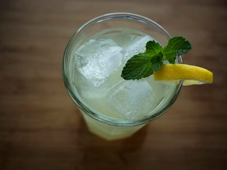 Tall glass of lemonade on wooden surface, garnished with fresh mint leaves and lemon slice