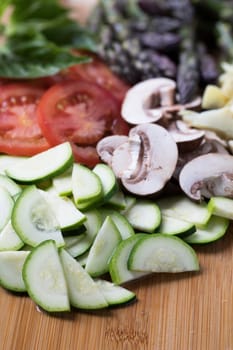 Fresh vegetable pizza toppings including zucchini, mushroom and tomato slices, and asparagus tips out of focus