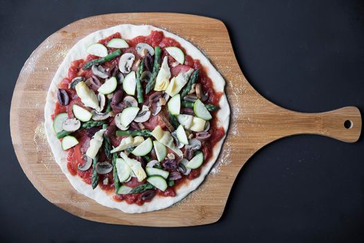 Homemade vegan pizza on pizza peel, uncooked and viewed from above.