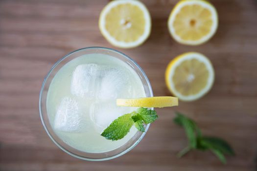 Top view of refreshing lemon drink garnished with mint and out of focus lemons on table