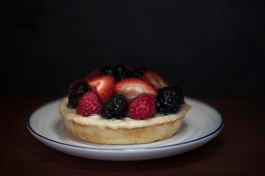 Small fruit topped cheesecake in small plate with dark background.