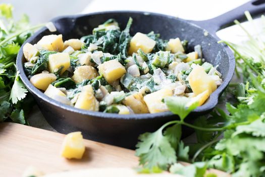 Iron pan with cooked potatoes and spinach for breakfast or taco filling.