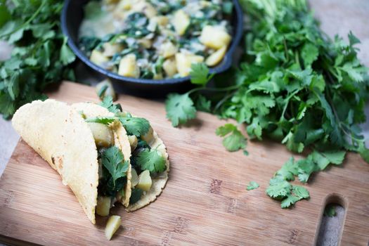 Two vegan soft tacos filled with potatoes and spinach and topped with cilantro.