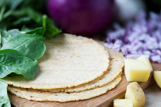 Corn tortillas surrounded by spinach, onions, and potatoes.  Ingredients for making vegan tacos.