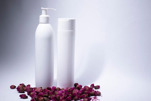 two white shampoo bottles and no label near a pile of little pink roses. body care and beauty concept. Copy space. High quality photo