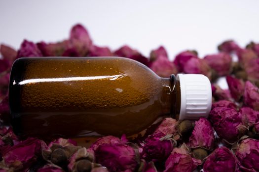 little liquid bottle with no label near a pile of little pink roses. body care and beauty concept. Copy space. High quality photo