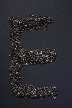 Letter 'E' written with chia seeds on gray background, top view, copy space.